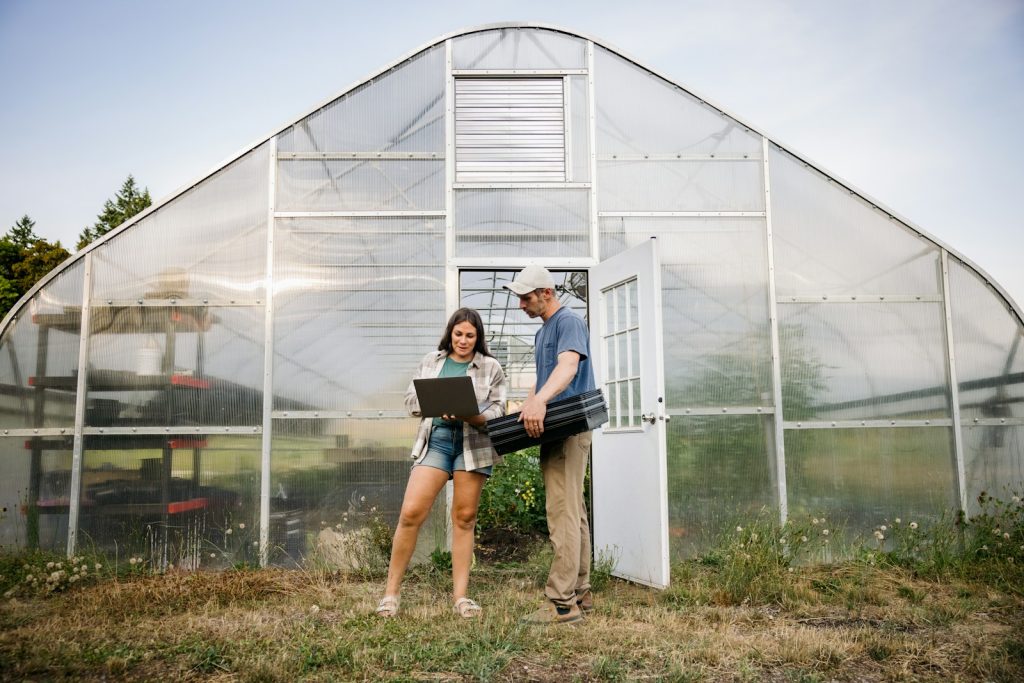 Two people working with a laptop outside greenhouse